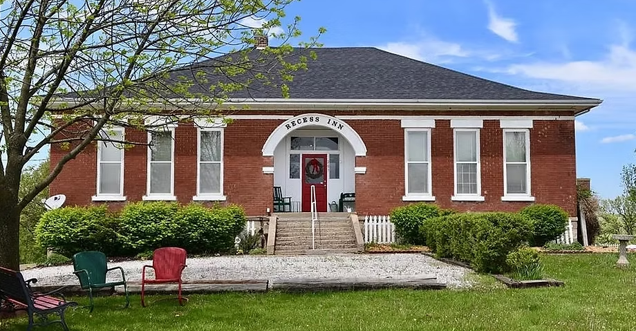 Brick building with white trim, a red door, and a sign that reads 