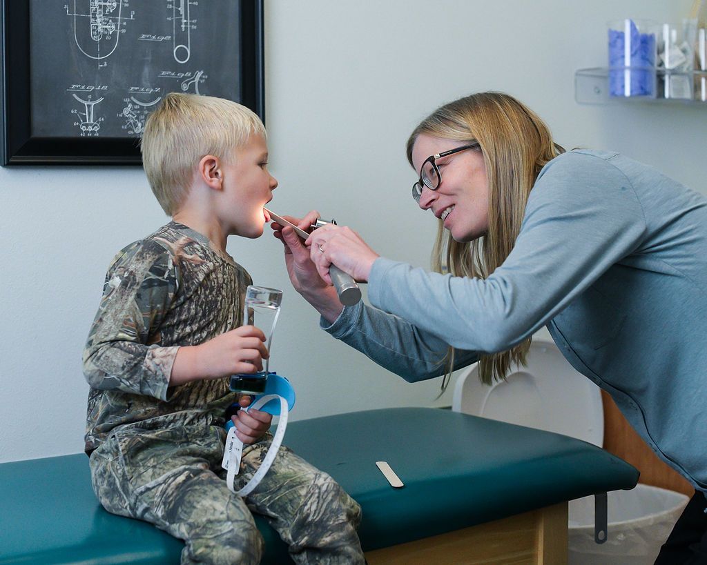 Doctor examining a young patient's throat with an otoscope in a medical office.