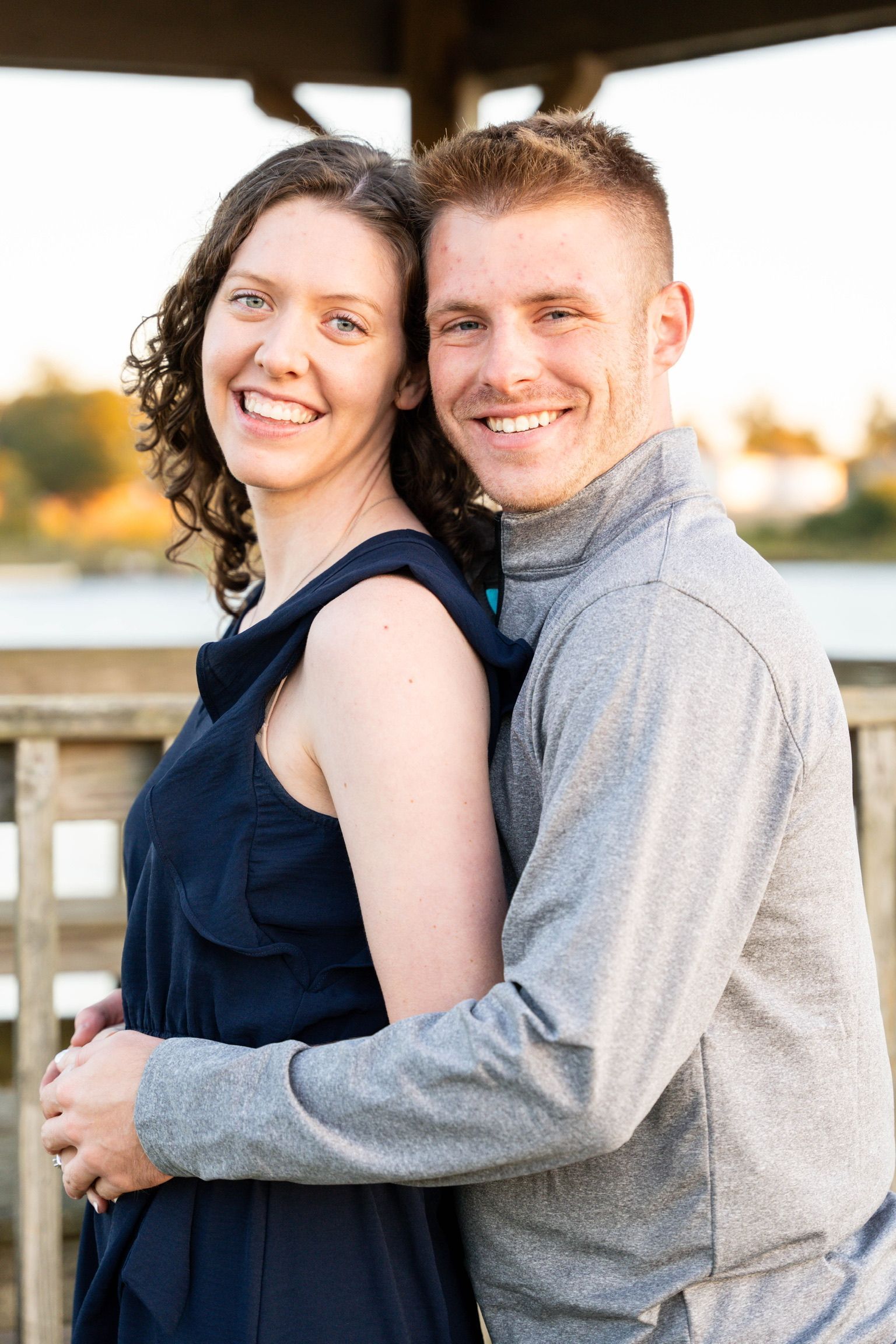 Smiling man with short blonde hair wearing a gray sweater and teal polo shirt against a dark background.
