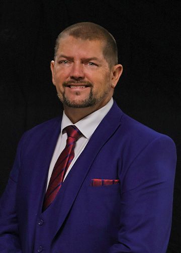 Man in suit smiles at camera against a black background.