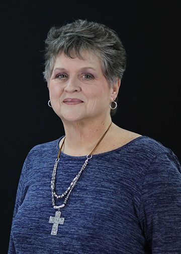 Woman with curly hair, wearing red top with white and blue spots, and hoop earrings.