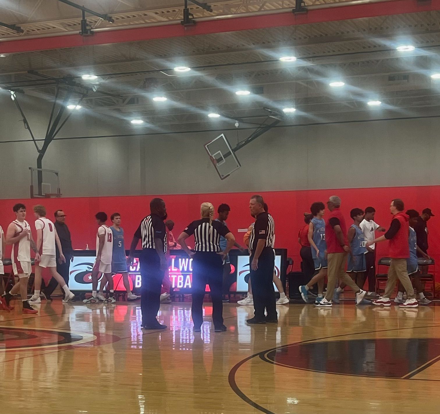 Basketball player in orange uniform dribbling the ball on a court, under bright lights.