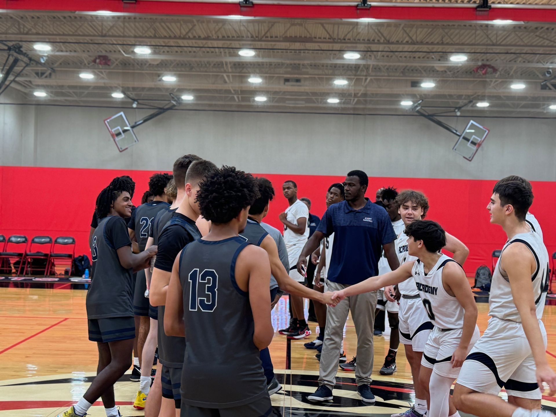 Basketball players huddle before a game. Two teams in jerseys shake hands in an indoor court.