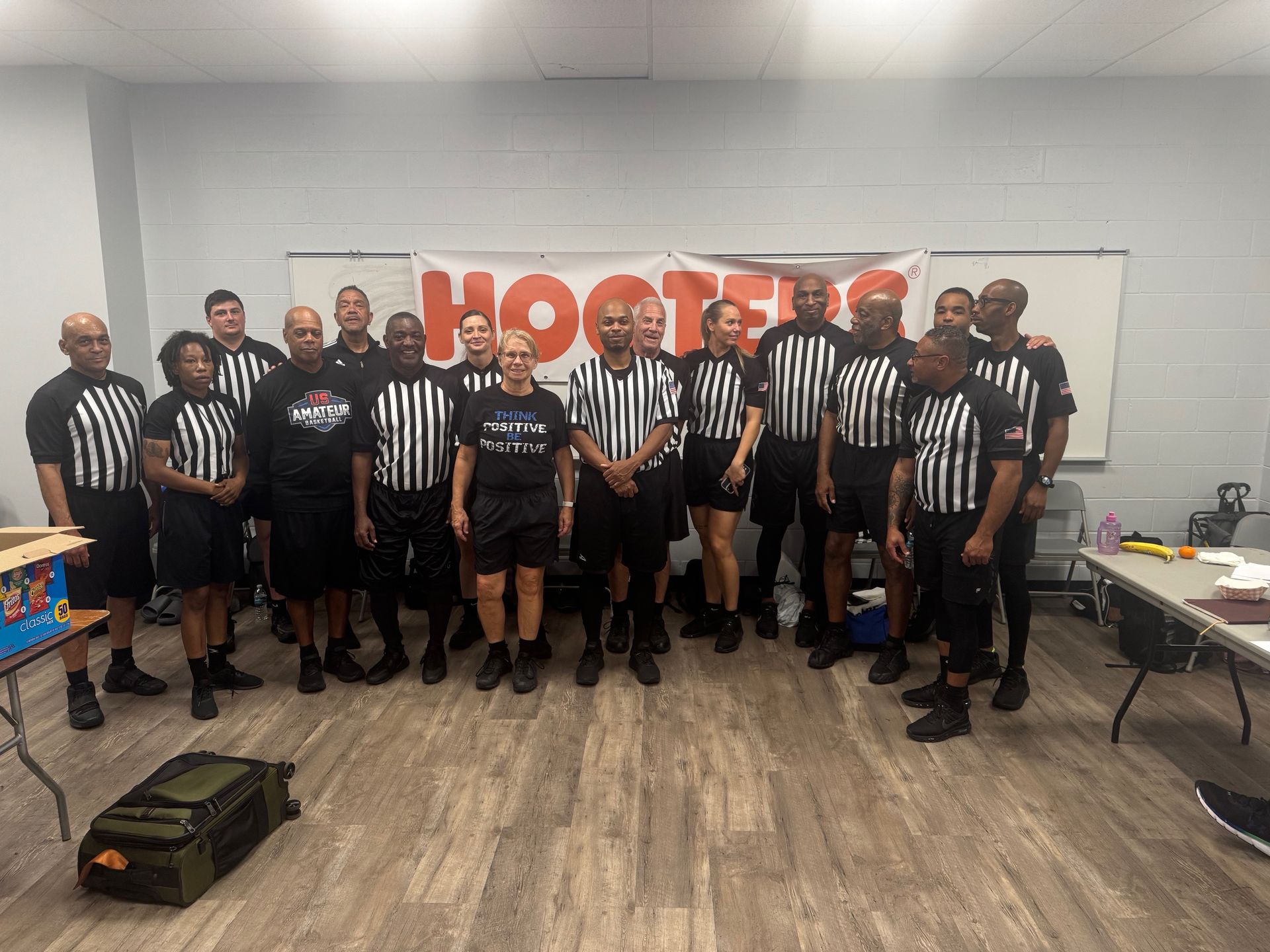 Group of people in referee uniforms standing in front of a Hooters banner.