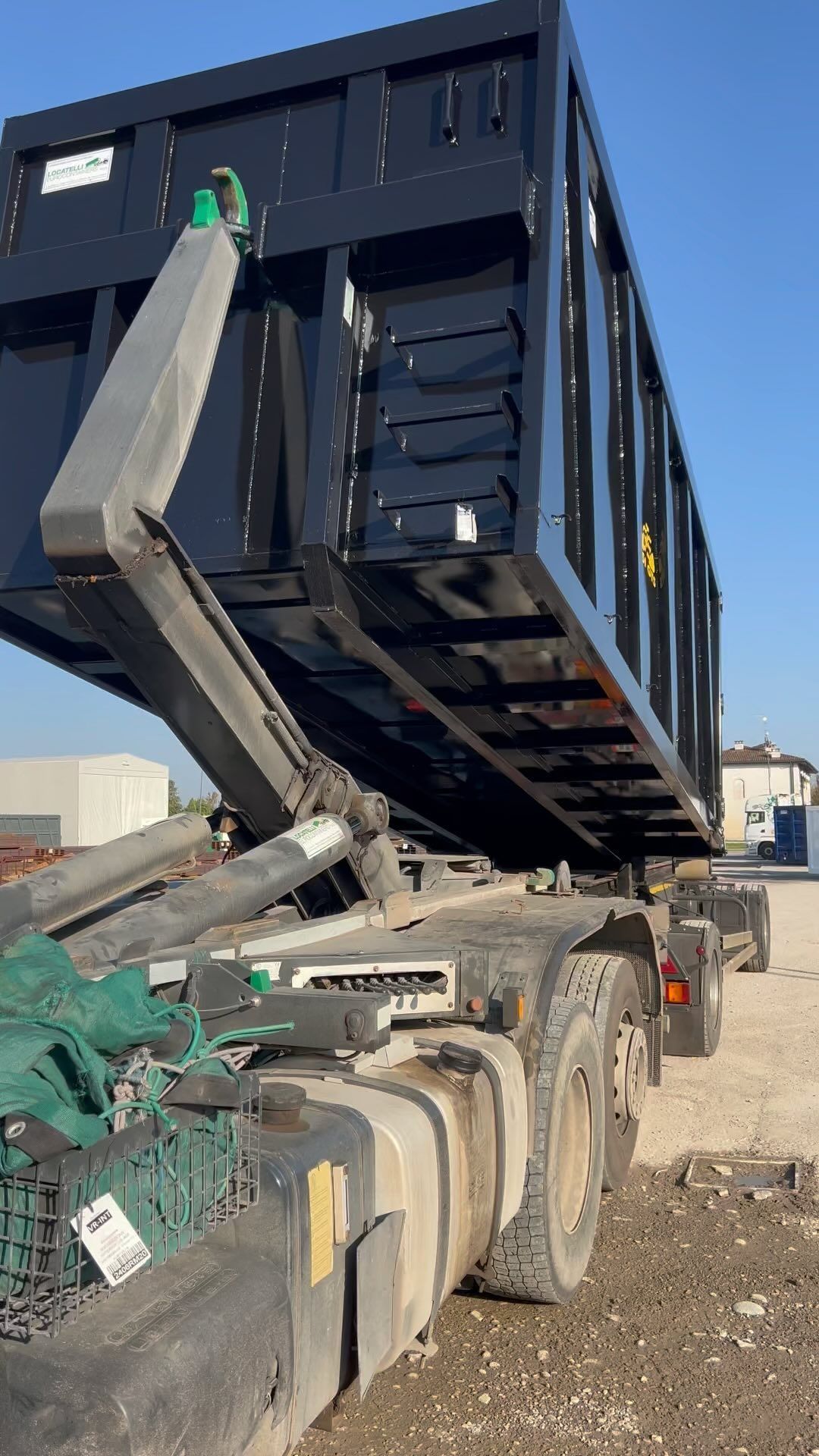 Un camion con cassone ribaltabile sta caricando un grande container nero.