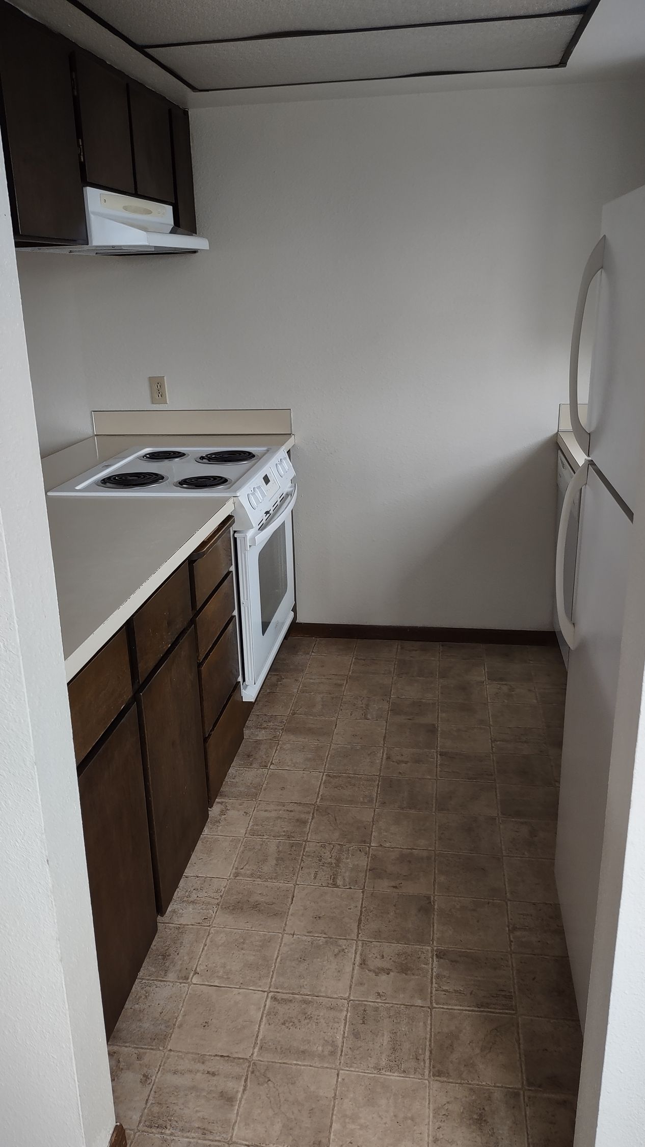 An empty kitchen with a stove , refrigerator , and cabinets.