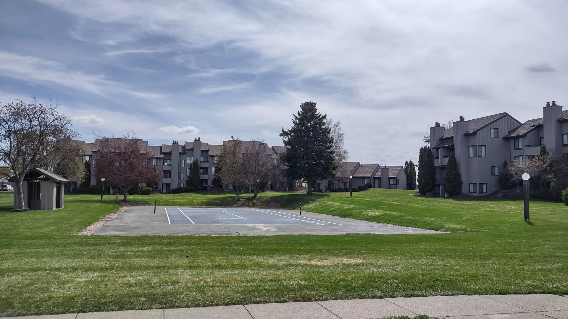 A basketball court in a park with buildings in the background.