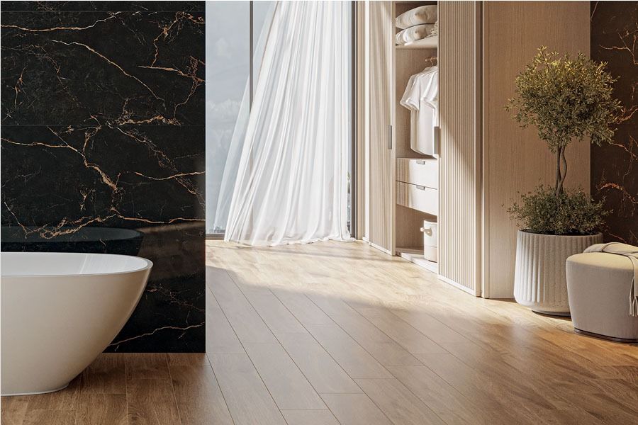 Baño con pared de mármol negro, bañera blanca, cortinas transparentes y piso de madera.