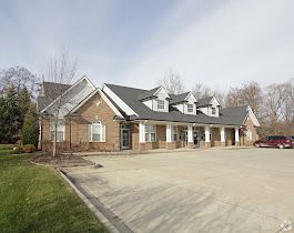 Exterior of a brick building with a glass door, address visible. A car is parked to the right.