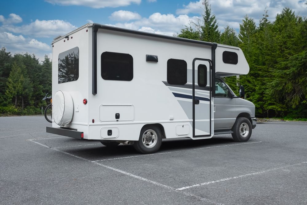 White camper van parked on asphalt with its side door open, surrounded by trees under a cloudy sky
