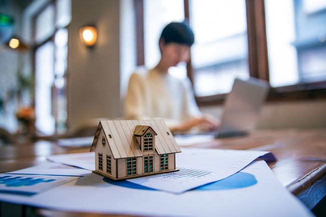 Una casa modelo está sobre una mesa al lado de un hombre que usa una computadora portátil.