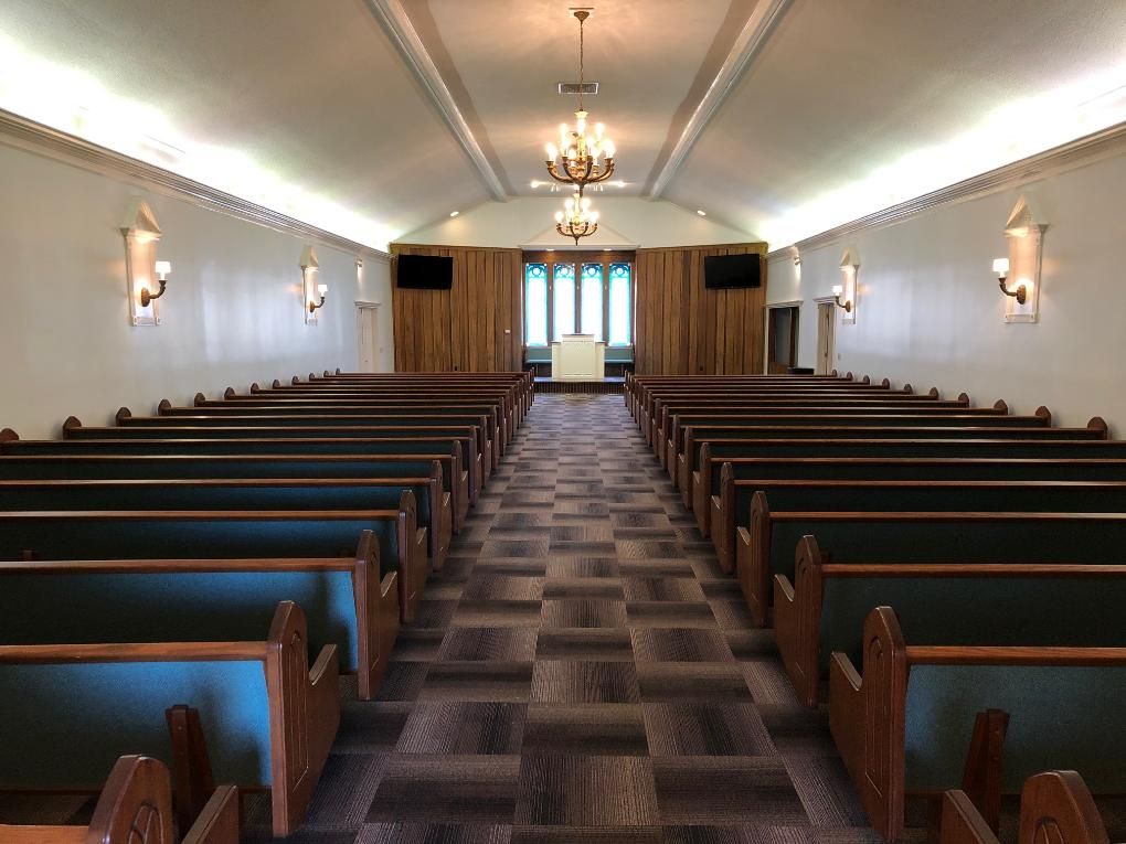 Interior of a funeral chapel with rows of wooden pews, altar, and stained-glass window.