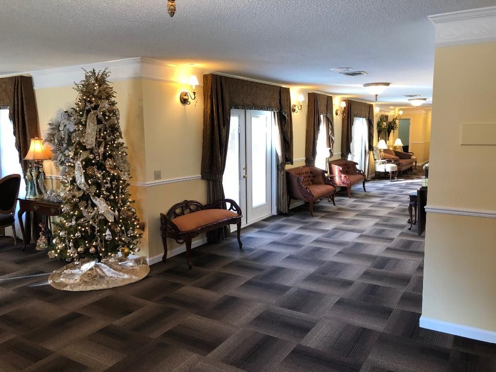 Spacious interior with a Christmas tree, seating, and windows. Neutral walls, patterned flooring, and formal decor.