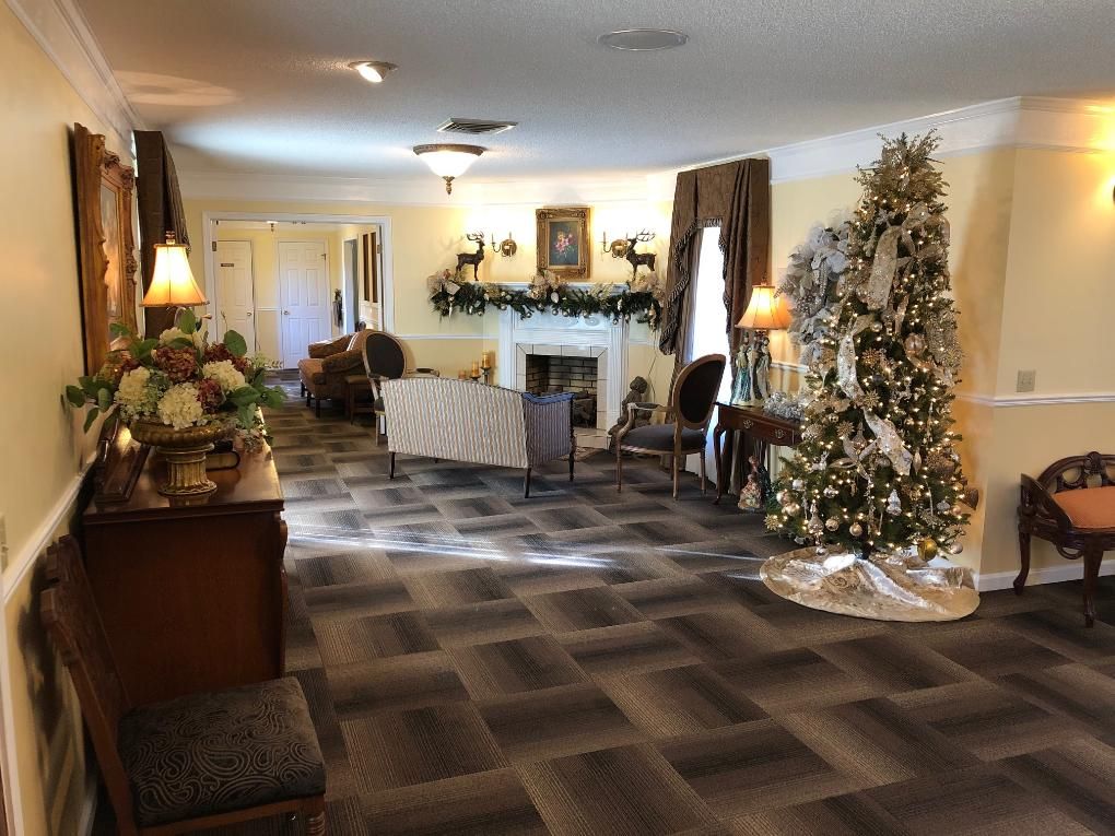 Elegant room with Christmas tree, fireplace, and furniture. Warm lighting and patterned carpet.