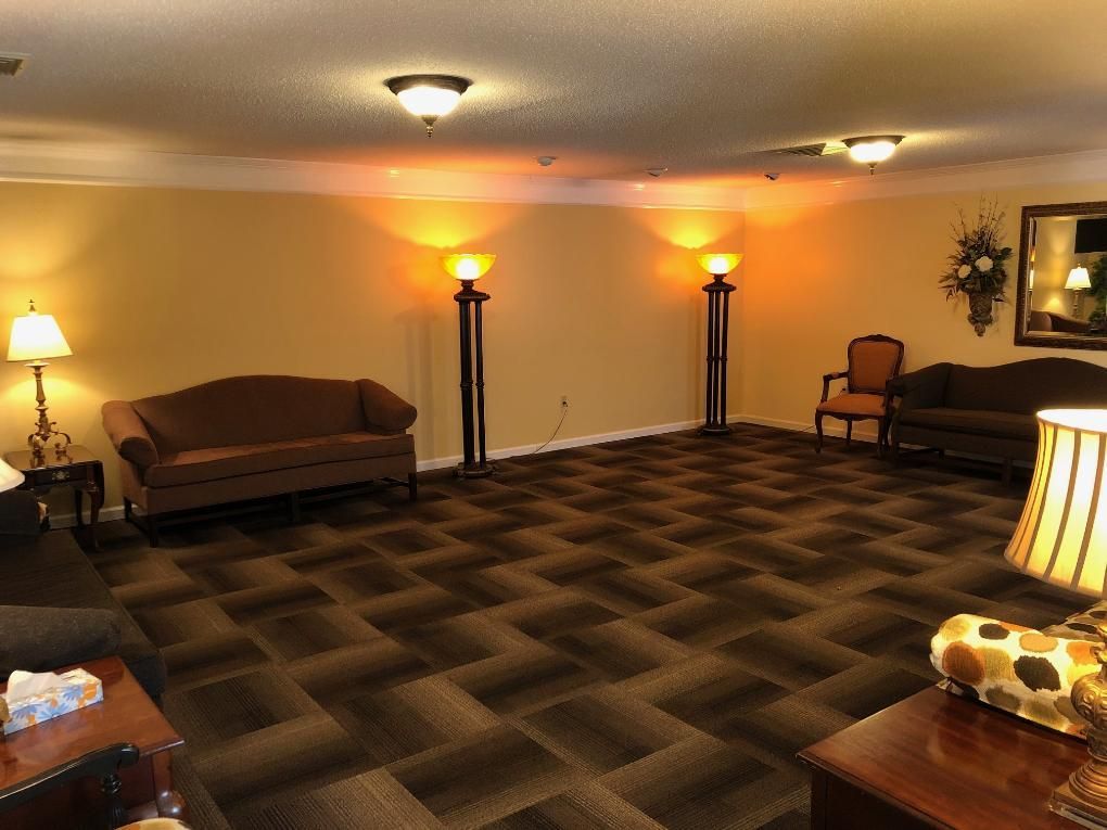 A spacious room with couches, chairs, and floor lamps. Brown carpet, light yellow walls, and ceiling lights.