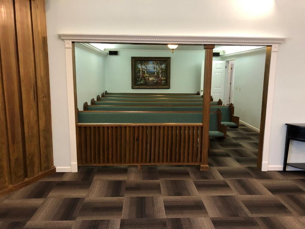 Interior view of a chapel with pews, a framed artwork, and a decorative wooden barrier.