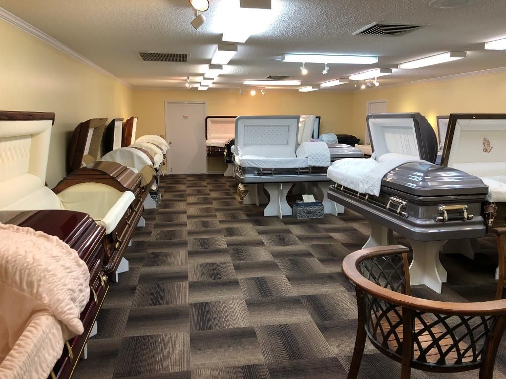 A room displays various caskets for sale, set up on stands.