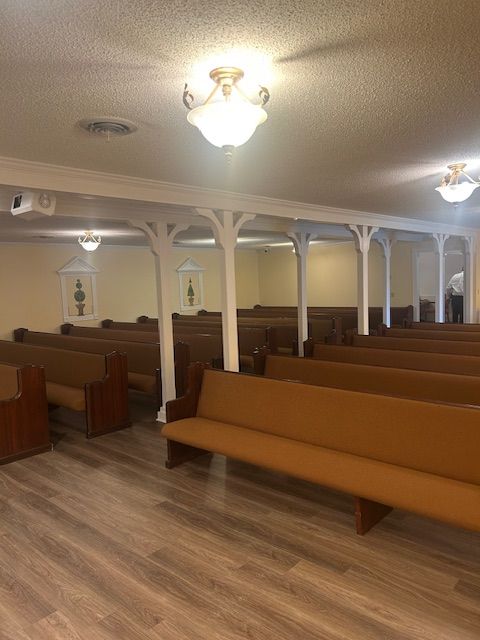 An empty church with wooden pews, white columns, and three decorative lights on the ceiling.