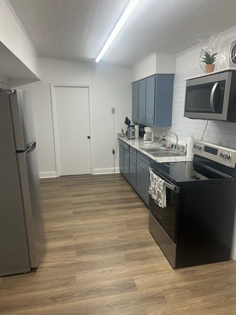Kitchen with blue cabinets, stainless steel appliances, and wood-look flooring.