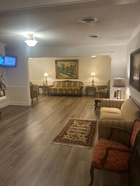 A funeral home waiting area with couches, lamps, artwork, and a decorative rug.