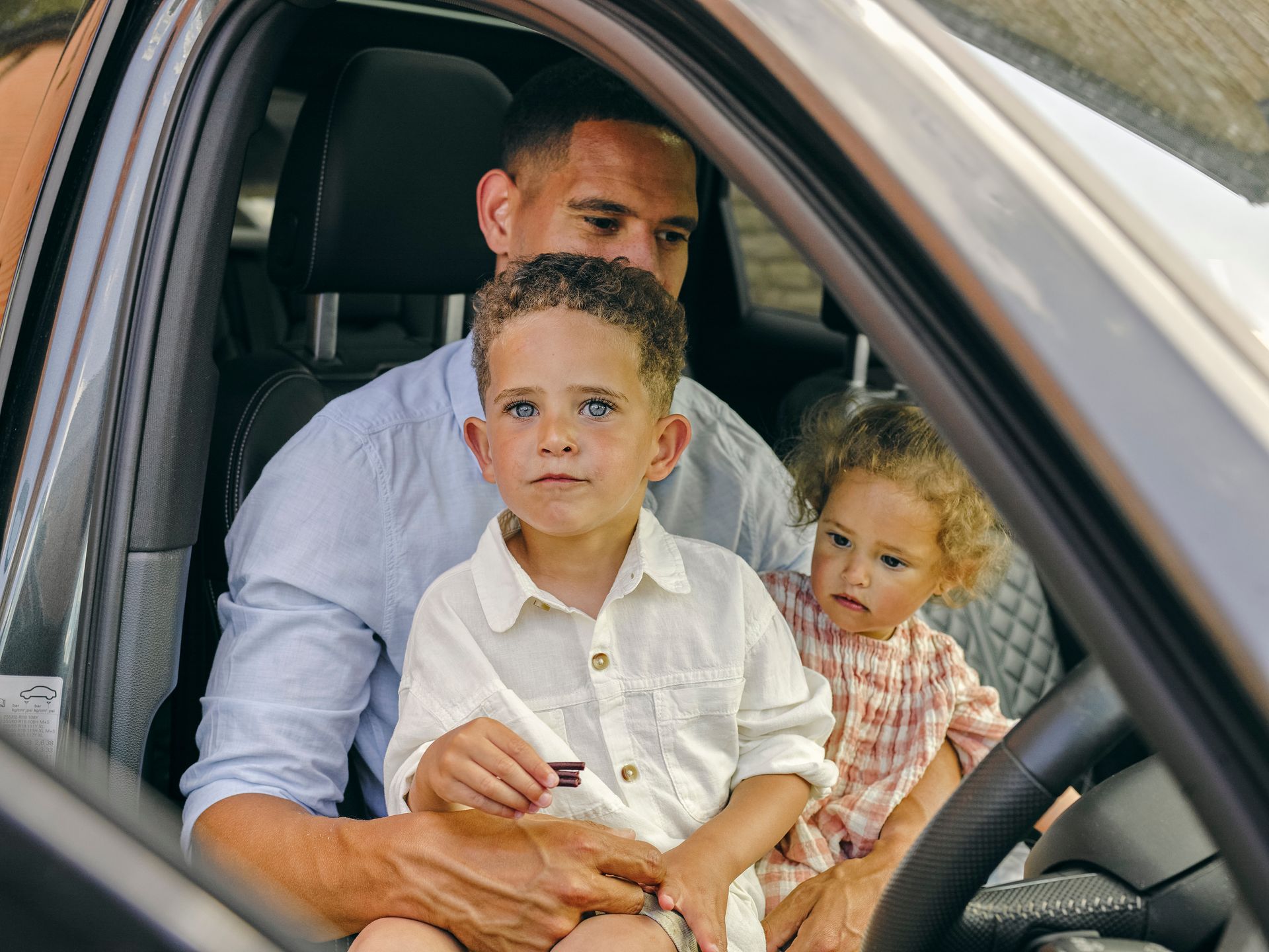 A man is sitting in a car holding two children.