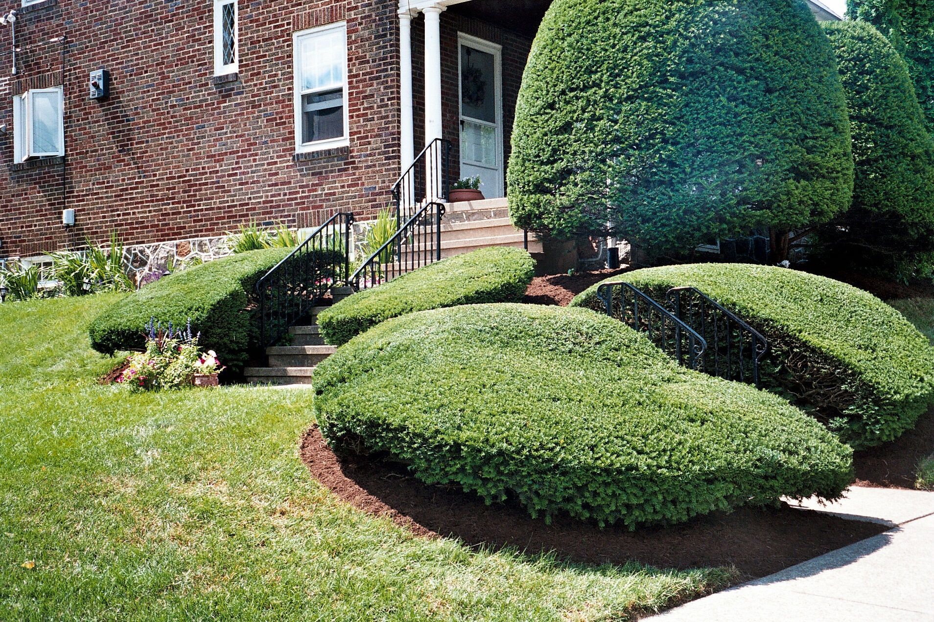 A brick house with a lush green lawn and bushes in front of it.