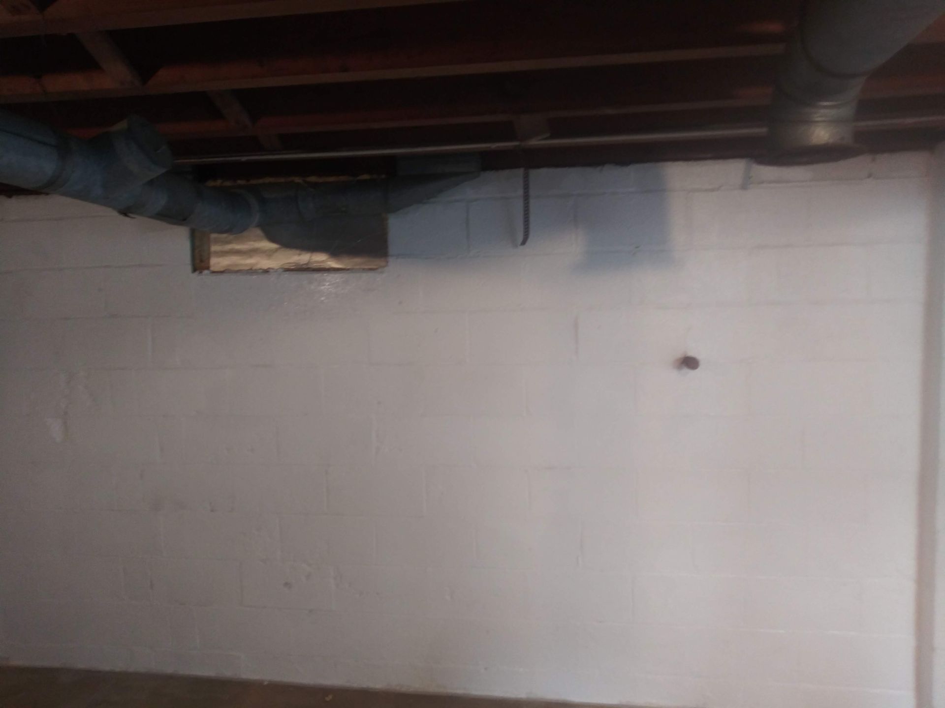 A white wall in a basement with pipes coming out of it.