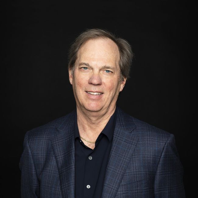 A man in a suit and black shirt is smiling for the camera.