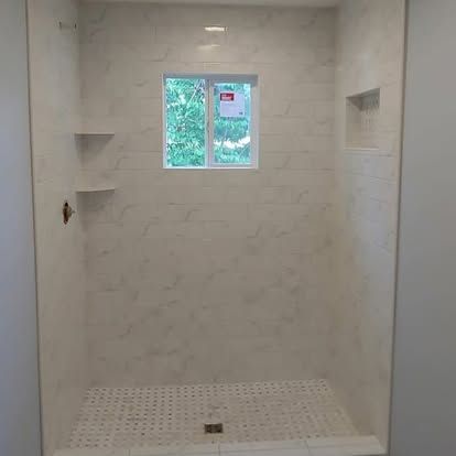 A shower stall with a window and shelves in a bathroom.