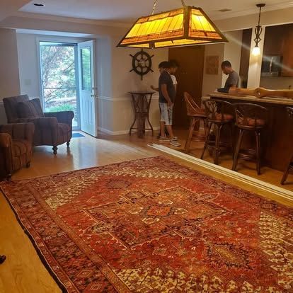 A living room with a large rug , chairs , stools and a lamp.