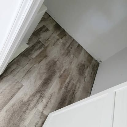 A corner of a room with a wooden floor and white cabinets.