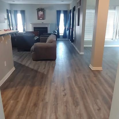 A living room with hardwood floors , a couch , chairs , and a fireplace.