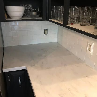 A kitchen with white counter tops , black cabinets , and a sink.
