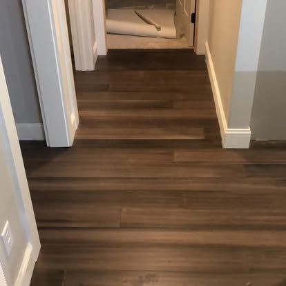 A hallway with hardwood floors leading to a bathroom.