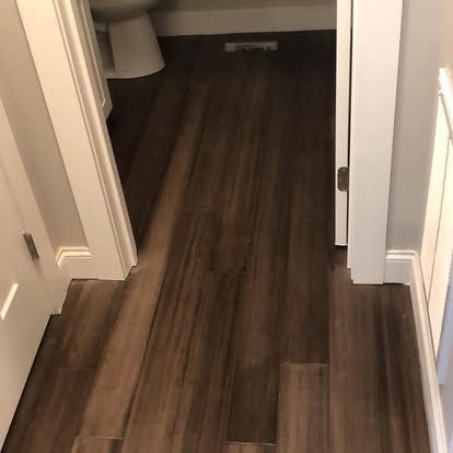 A hallway with hardwood floors leading to a bathroom.
