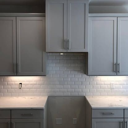 A kitchen with gray cabinets and white counter tops.