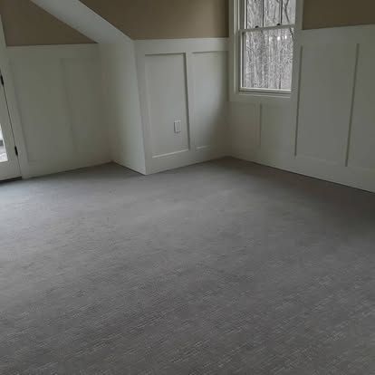 An empty room with a gray carpet and a window.