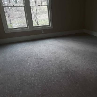 An empty room with a gray carpet and two windows.