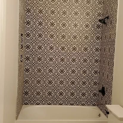 A bathroom with a bathtub and a shower with a black and white tile wall.