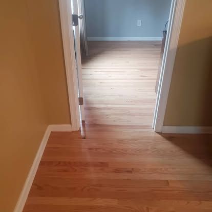 A hallway with hardwood floors and a door leading to a bedroom.