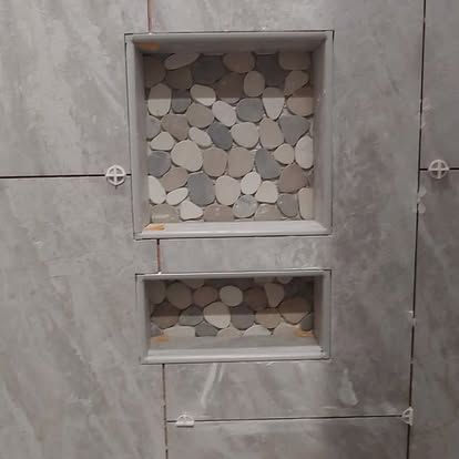 A shower niche with a mosaic of rocks on the wall.
