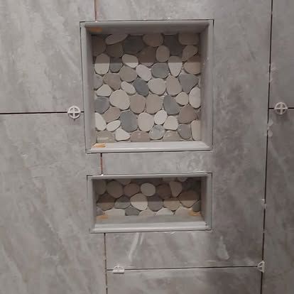 A shower niche with a mosaic of rocks on the wall.