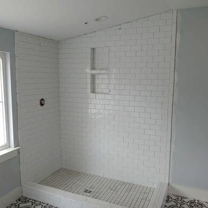 A shower stall with white tiles and a window in a bathroom.