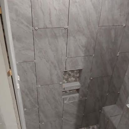 A shower stall with gray tiles being installed in a bathroom.