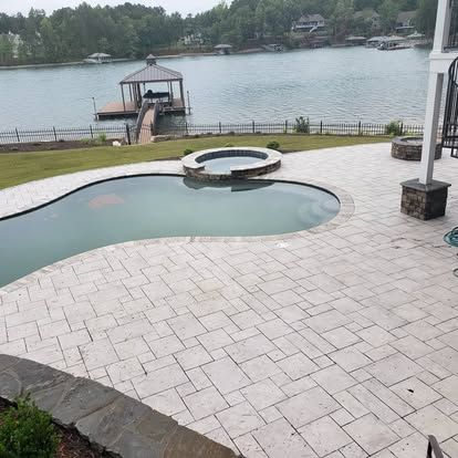 A large swimming pool is surrounded by a patio and a lake.