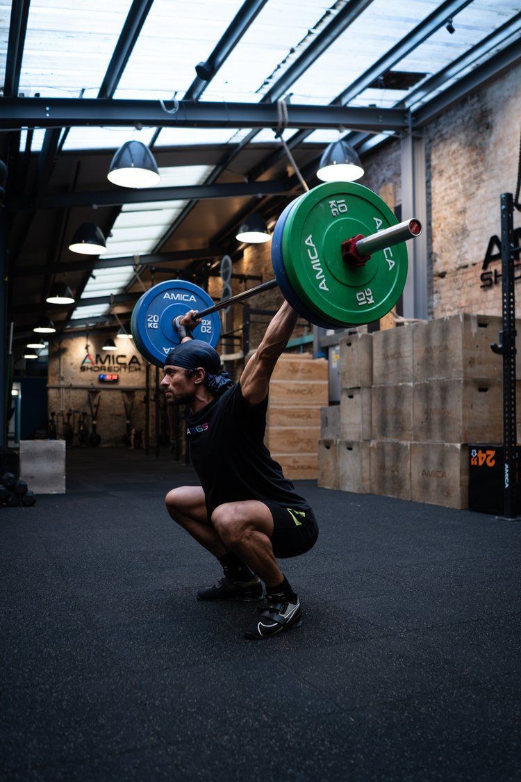 A man is squatting down with a barbell over his head in a gym.
