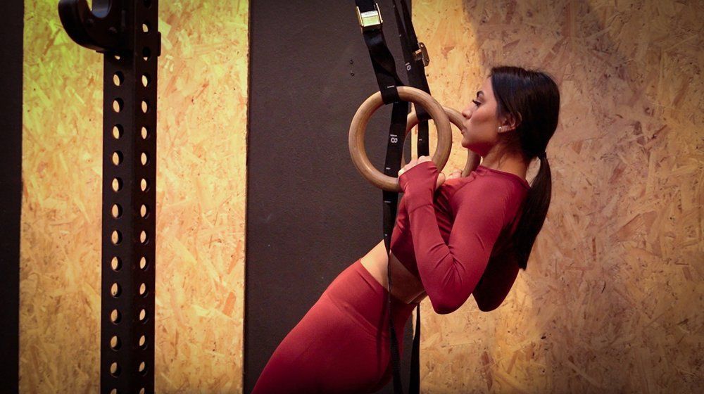 A woman is doing a pull up on gymnastic rings in a gym.