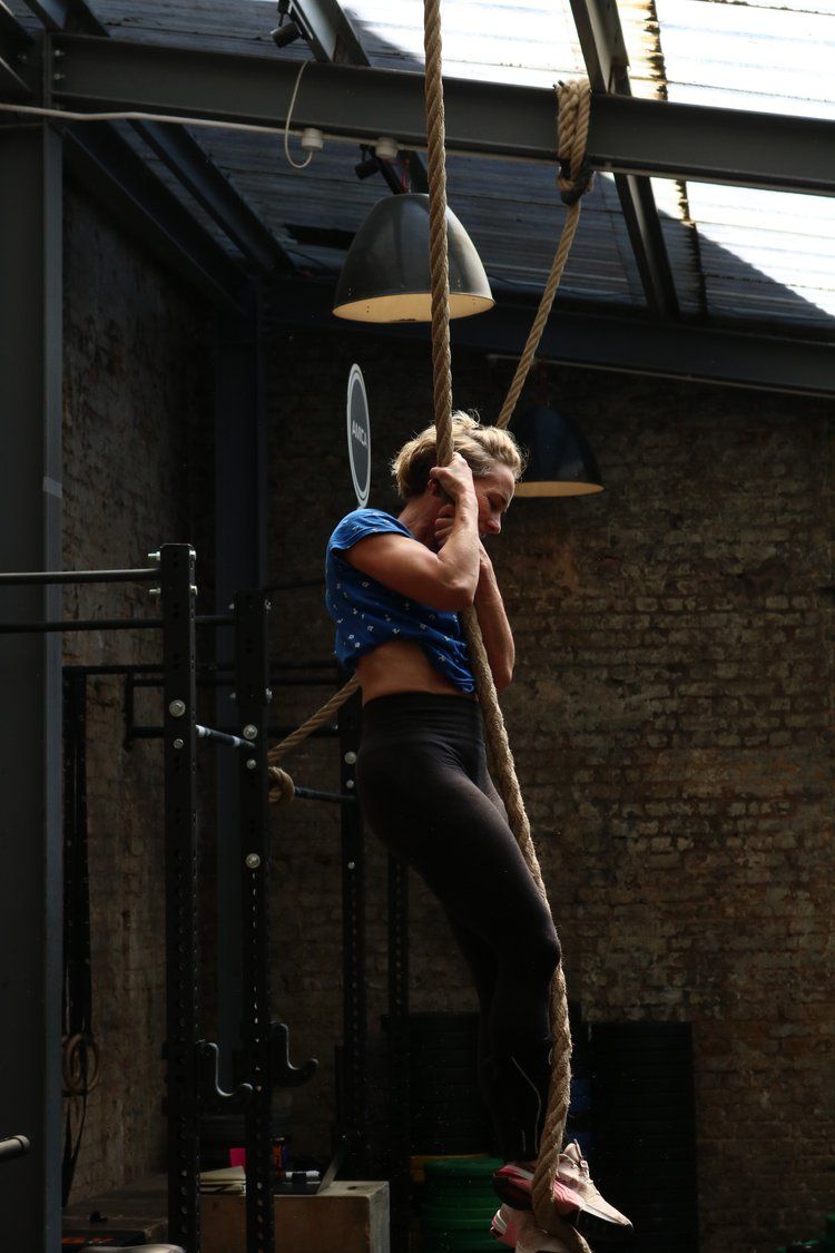 A woman is climbing a rope in a gym