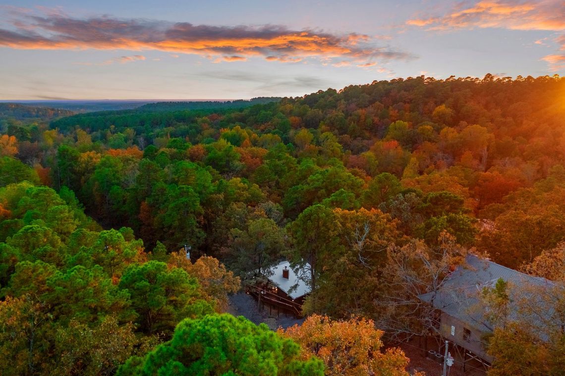 An aerial view of a house in the middle of a forest at sunset.