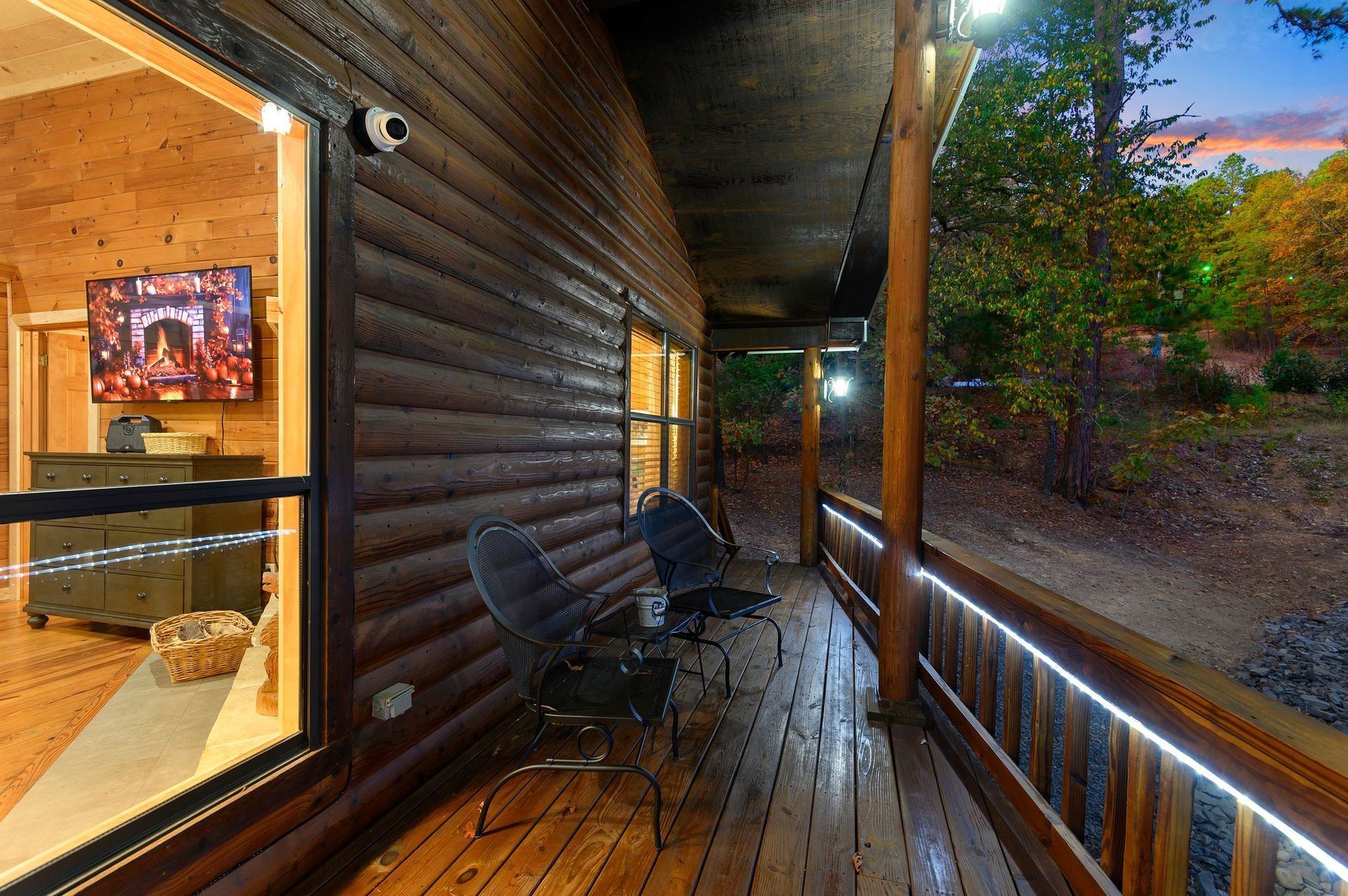 A wooden deck with chairs and a television on the side of a log cabin.